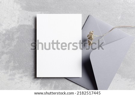 Invitation or greeting card mockup with envelope and dry flowers decoration over grey concrete background