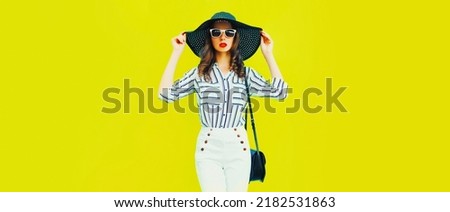 Portrait of beautiful woman model wearing black round straw summer hat, handbag and white striped shirt on yellow background