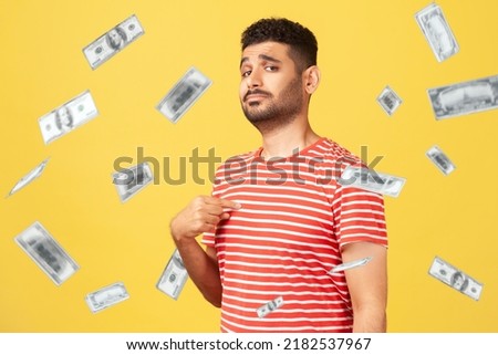 This is rich man. Portrait of arrogant self-confident man pointing at chest, looking proud and egoistic. money falling and he is rich. indoor studio shot isolated on yellow background