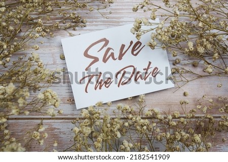 Save the Date text on paper card with flower decoration on wooden background