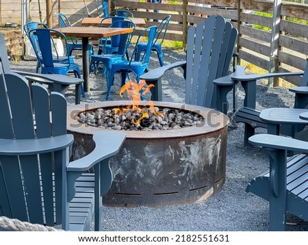 Close up view of adirondack chairs circling a fire pit filled with stones inside an outdoor patio area at a restaurant