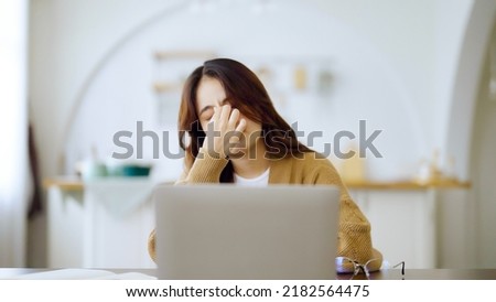 Overworked tired young asian woman feeling headache, having eyesight problem after computer laptop work. Stressed adult business woman suffering from fatigue rubbing dry eyes at home Royalty-Free Stock Photo #2182564475