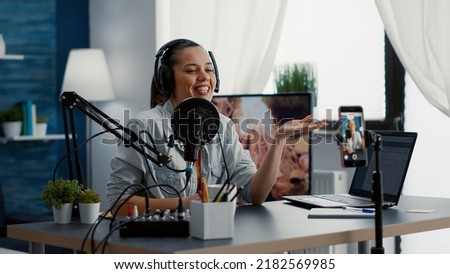 Influencer putting on headphones while recording video with phone and talking to audience. Joyful internet star filming daily vlog while speaking to public about her day. Royalty-Free Stock Photo #2182569985
