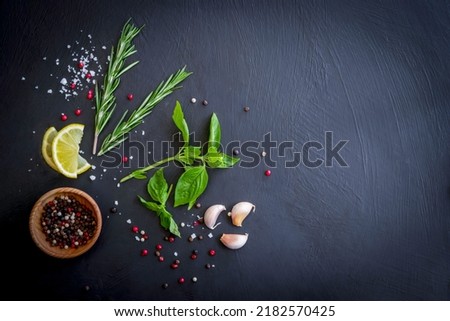 spicy green herbs as ingredients for cooking, consisting of red, black, white, pepper seeds, rosemary, basil, lime, and salt on a slate table. food background dark tone top view with copy space