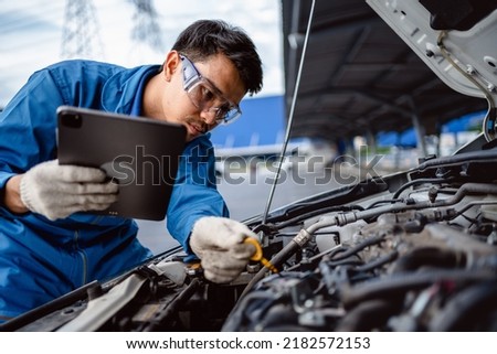 Automotive mechanic repairman using tablet and pulling dipstick to checking engine oil level engine in the engine room, check the mileage of the car, oil change, auto maintenance service concept. Royalty-Free Stock Photo #2182572153