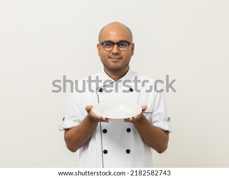 Smiling Young handsome asian man chef in uniform holding empty plate delicious dish menu good taste on isolated. Cooking indian man Occupation chef or baker People in kitchen restaurant and hotel.
