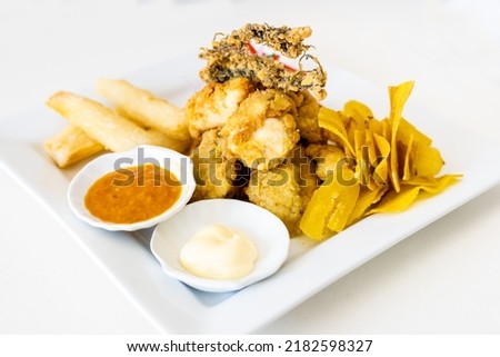 Peruvian food: chicharron de pescado or fish cracklings with fried cassava and onion salad with chili, served on a white plate. White background