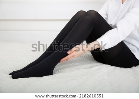 Beautiful long female legs in stockings. Girl putting on stockings at home in a white room. Black tights. Varicose veins prevention. Woman body in underwear.
