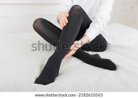 Black compression stockings on a woman in a white room. Black tights. Girl putting on stockings at home. Beautiful female legs. Royalty-Free Stock Photo #2182610565