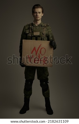 Anti-war protest. Studio shot of a brave soldier in camouflage standing on a khaki background with a sign "No War". No War concept. 