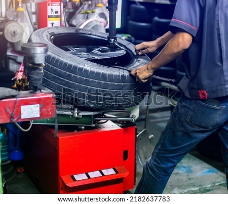 Selective focus to engineer balancing car wheel on balancer in workshop. Mechanic with pneumatic wrench unscrews the wheel. Mechanic repairing a car wheel. Male mechanic at a car garage fixing a wheel Royalty-Free Stock Photo #2182637783