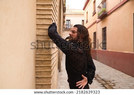 Long haired man dancing flamenco with black shirt and red roses. He makes dancing postures with his hands in a typical narrow street of Seville. Flamenco dance concept cultural heritage of humanity.