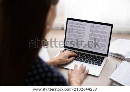 Back rear close up view focused young businesswoman working on electronic documents in computer editing application. Concentrated professional journalist writing article or student writing essay.