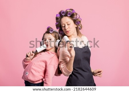Two beautiful women mother and daughter sing their favorite songs into pretend microphone, fool around listening to music, have hair curlers on their heads, joy shared relationship bond parental love.