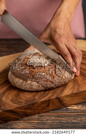 Hands of a woman holding and cutting a rustic sourdough bread with knife - stock photo