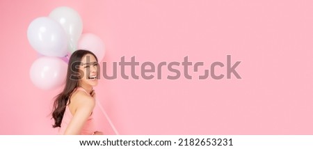 Happy asian woman holding balloons looking at camera in excitement Expressive facial expressions Beautiful girl enjoy holiday and celebrate for party or special day Use for advertising Pink background
