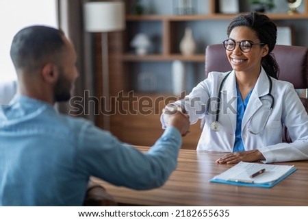 Friendly young african american lady doctor smiling and shaking male patient hand, cheerful black woman therapist greeting middle eastern guy at her clinic, outstretching hand, copy space Royalty-Free Stock Photo #2182655635