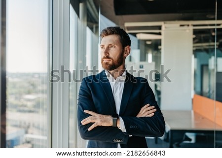 Successful businessman in formal wear standing with folded arms in modern coworking office and looking through window, thinking about startup, planning new projects, waiting for meeting Royalty-Free Stock Photo #2182656843