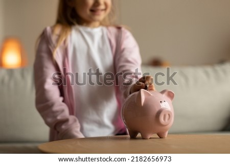 Unrecognizable Little Girl Putting Coin In Piggybank Raising Personal Money Savings At Home. Cropped Shot Of Kid Investing Cash. Bank Services And Finances Safety Concept. Shallow Depth Royalty-Free Stock Photo #2182656973