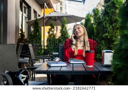 Young woman enjoying coffee sitting on the terrace of a cafe on the street of a modern city. A man sits at a table and uses a laptop outdoors.