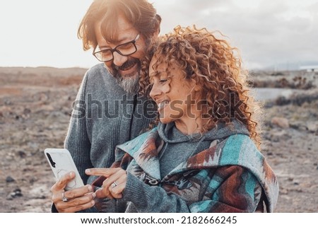 Man and woman using mobile phone app outdoor smiling and enjoying technology connection. Happy couple communicate with mobile cellular together. Tourist use online map and touristic infos. Leisure Royalty-Free Stock Photo #2182666245