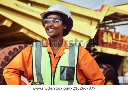 A young African woman mine worker is standing in front of a large haul dump truck wearing her personal protective wear Royalty-Free Stock Photo #2182667079
