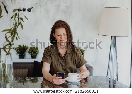 beautiful young woman sitting at home, browsing pictures on smartphone, focus on device screen. online job concept