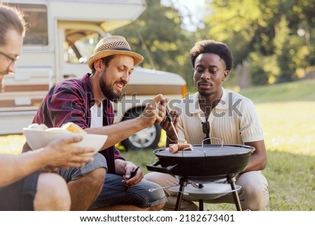 A bearded middle-aged guy is preparing a barbecue for friends. A group of college boys hang out together. RV trip