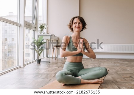 Pretty young brunette woman practicing yoga at home . Caucasian cute girl looking away and smiling wearing green sportswear sitting on the floor. Concept of leisure, relaxation, workout  Royalty-Free Stock Photo #2182675135