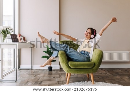 Picture of caucasian brunette woman having fun at home . Dark-haired young girl in headphones listening music sitting on the chair. Home mood, lifestyle 