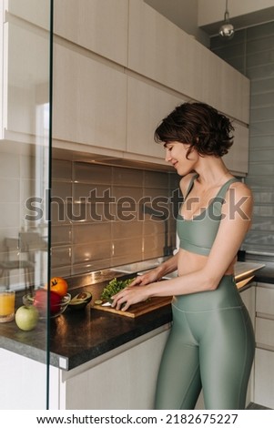 Pretty young sporty woman cooking in the kitchen . Picture of attractive brunette girl staying at home looking and doing salad wear sportswear. Healthy lifestyle, home comfort concept 