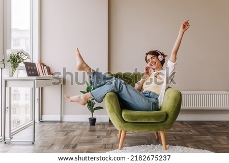 Caucasian beautiful woman smiling at home in headphones . Short brunette hair young girl wearing blue jeans listen music at home. Use technology, lifestyle concept  Royalty-Free Stock Photo #2182675237
