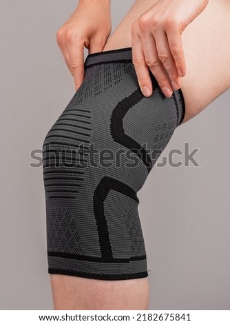 Woman putting on knee brace to support painful leg or heal from injury. Tool used by athlete after trauma for doing sport. Health problems, medical conditions concept. High quality photo Royalty-Free Stock Photo #2182675841