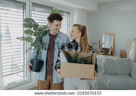 Cheerful young couple in their new apartment, carrying boxes. Conception of moving.