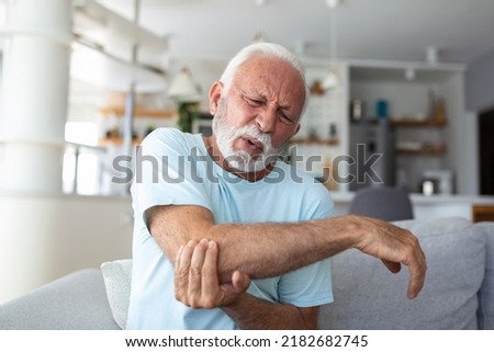 Senior man with arm pain.Old male massaging painful hand indoors. Old man hand holding his elbow suffering from elbow pain. Senior man suffering from pain in hand at home. Old age, health Royalty-Free Stock Photo #2182682745