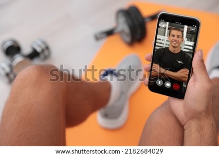 Man having workout with personal trainer via smartphone at home, closeup Royalty-Free Stock Photo #2182684029