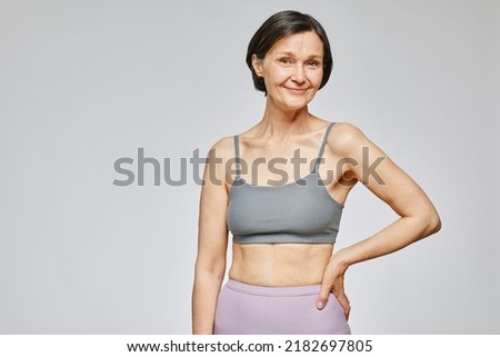 Minimal waist up portrait of smiling mature woman wearing neutral underwear against grey background, body positivity concept, copy space Royalty-Free Stock Photo #2182697805