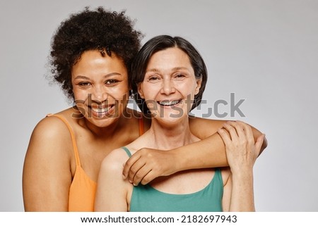 Minimal waist up portrait of two real women embracing and smiling happily against grey background Royalty-Free Stock Photo #2182697943