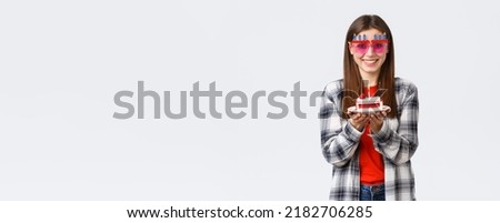 People lifestyle, holidays and celebration, emotions concept. Cheerful cute girl in glasses holding birthday cake, celebrate b-day, making wish to blow lit candle, white background