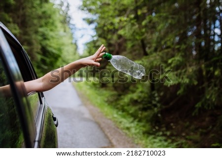 Woman's hand throwing away plastic bottle from car window on the road in green nature, environmental protection, global warming concept Royalty-Free Stock Photo #2182710023