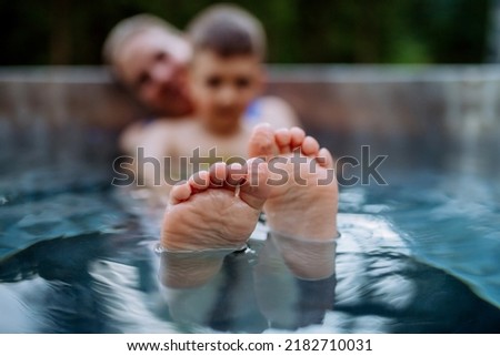Mother with her little son enjoying bathing in wooden barrel hot tub, focus on feet.