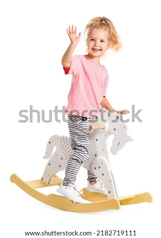 Cute little girl with rocking horse waving hand on white background Royalty-Free Stock Photo #2182719111