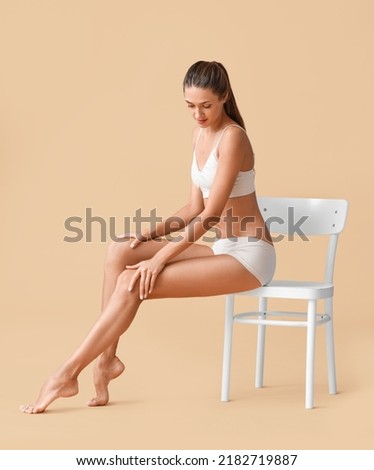 Young tanned woman sitting in chair on beige background