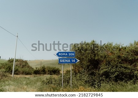 A closeup of a blue direction sign in a field leading to Roma and Siena