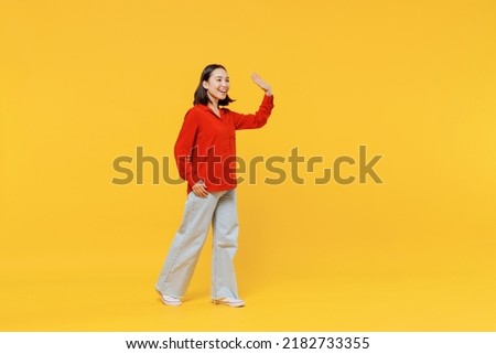 Full size body length cheerful young woman of Asian ethnicity 20s in casual clothes look camera go move meet greet waving hand as notices someone isolated on plain yellow background studio portrait Royalty-Free Stock Photo #2182733355