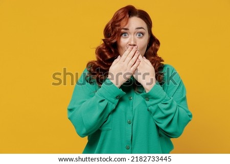 Secret bright vivid young ginger chubby overweight woman 20s years old wears green shirt cover mouth with hand isolated on plain yellow background studio portrait. People emotions lifestyle concept Royalty-Free Stock Photo #2182733445