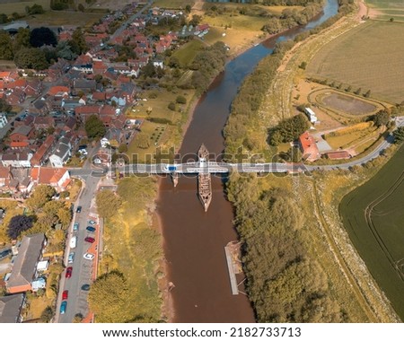 An aerial shot of a town by a river with a boat passing under the bridge