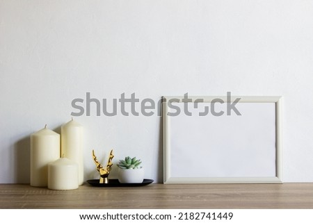 White photo frame with white candlelight's and green leaves over the wooden table. 