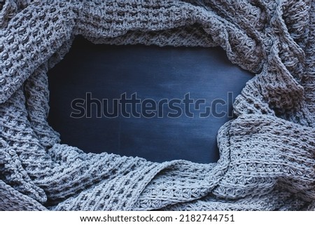 Grey woven blanket crumpled and framed over a dark toned black wooden background. Shot from above top view with free space for text for background. 