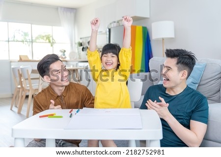 Asian attractive LGBTQ gay family teach young girl kid draw picture. Handsome male couple look at little adorable child daughter play and coloring book in living room, enjoy parenting activity at home